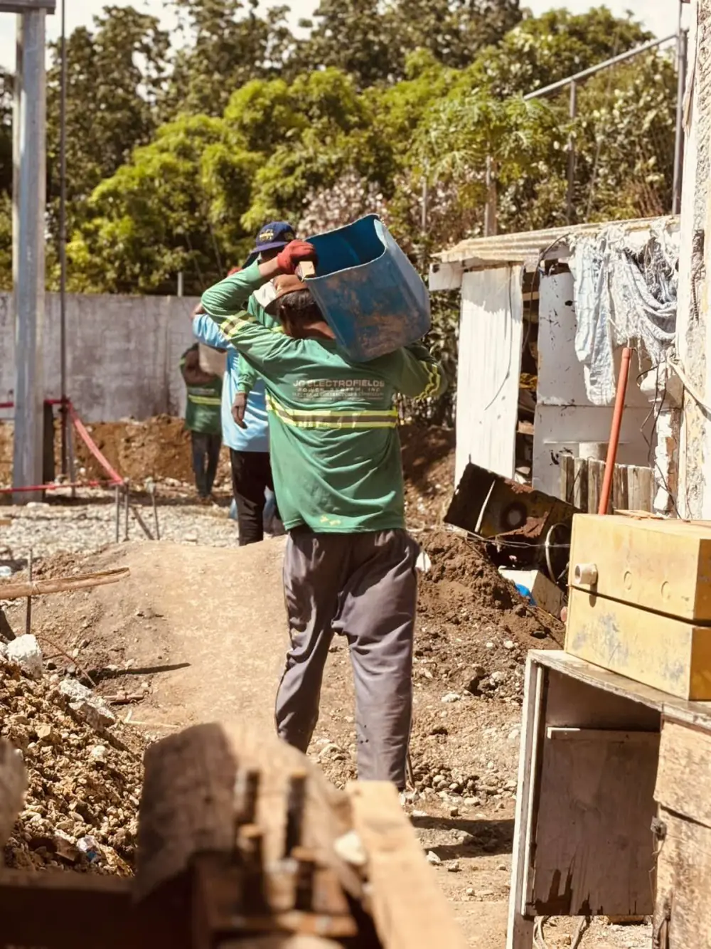 A JC Electrofields worker hauling a bucket of material across a sunlit construction site