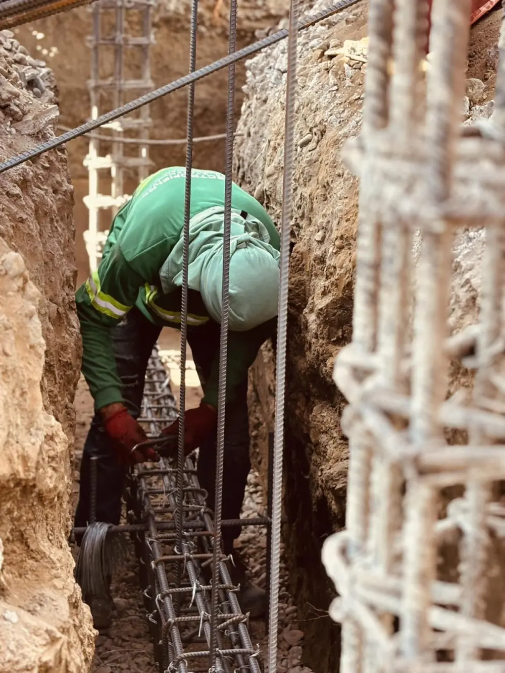 A JC Electrofields worker tying a steel rebar cage inside a deep foundation trench