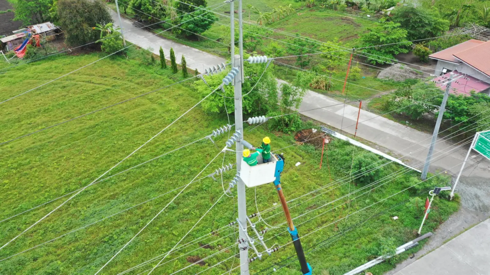 Aerial of a bucket truck servicing a distribution line over green fields