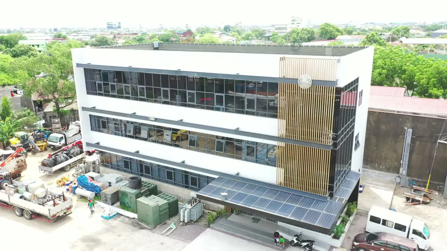 Aerial orbit of the JC Electrofields headquarters in Valenzuela City — a glass-and-concrete building with a rooftop canopy and equipment yard