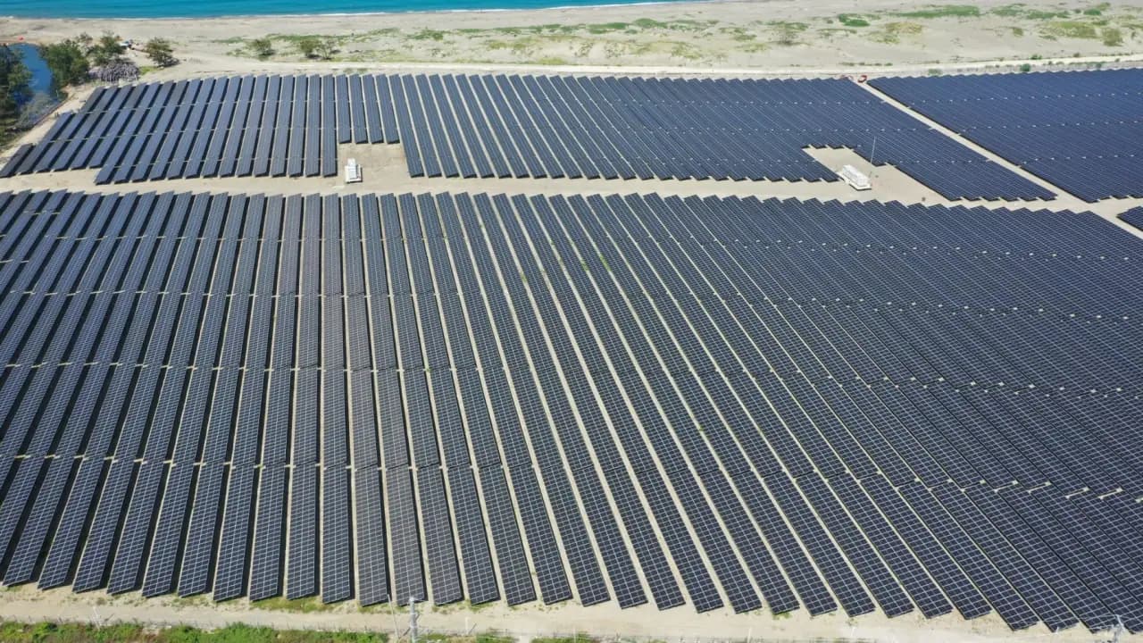 Aerial of a coastal solar farm, panels reaching toward the shoreline