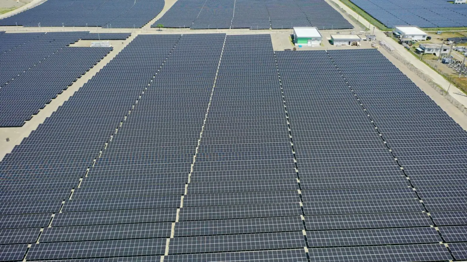 Aerial of dense rows of solar panels beside white control buildings