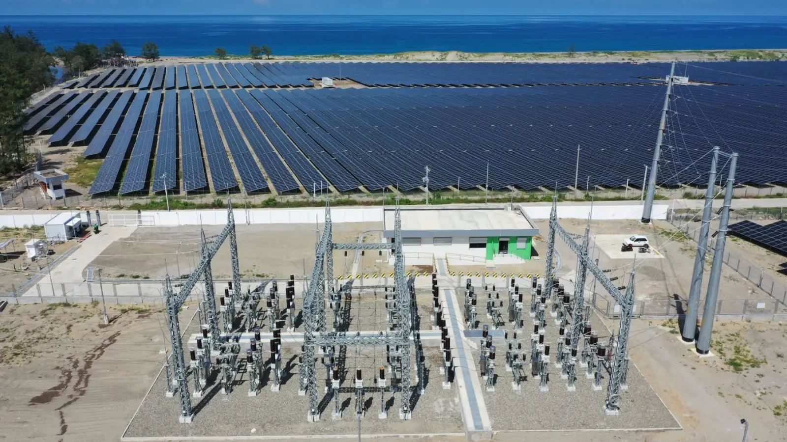 Aerial of a coastal solar farm and substation switchyard built by JC Electrofields, the sea on the horizon
