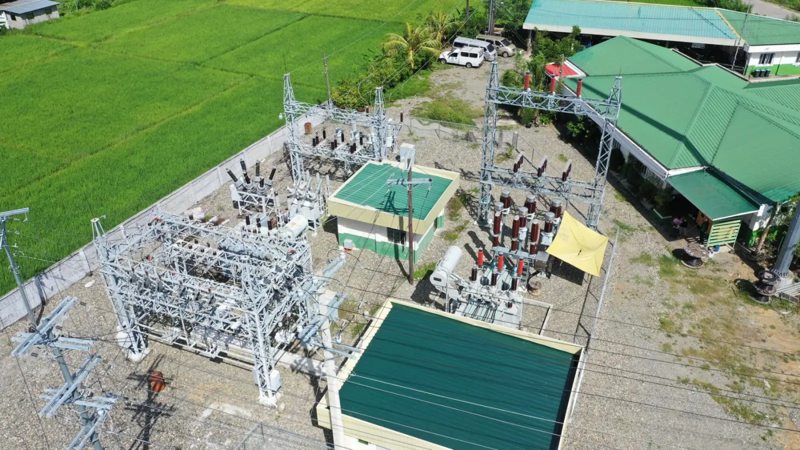 Aerial of a substation beside bright green rice paddies and rural houses