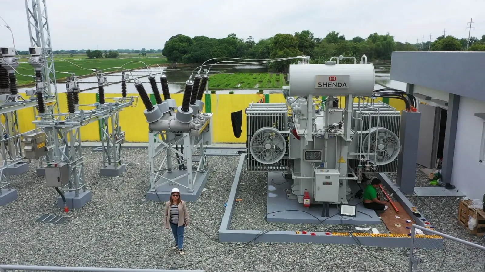 Engineer standing beside a SHENDA power transformer at a substation, rice fields behind